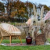 Stylowy fotel retro w beżowej tapicerce z drewnianymi nogami, ustawiony na wzorzystym dywaniku w plenerze. Aranżacja ozdobiona suszonymi trawami, wazonami z kwiatami oraz wiklinowym koszem, tworzy rustykalny i boho klimat. Idealna dekoracja na śluby, wesela i eventy w Wrocławiu. Wynajmij tę wyjątkową scenografię na rent4events.pl lub rent4weddings.pl, aby dodać uroku i naturalnego piękna Twojej uroczystości - rent4events.pl wypożycz wrażenia, rent4wedding.pl zachowaj wspomnienia. Fot. @masterfilmwroclaw.