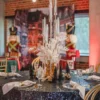 Świąteczne dekoracje idealne na grudniowy ślub, bankiet czy event we Wrocławiu. Okrągły stół z czarnym, brokatowym obrusem udekorowany jest eleganckimi białymi serwetkami na przezroczystych podtalerzach, złotymi sztućcami i przezroczystymi kieliszkami kryształowymi. Na stole znajduje się wysoka, złota aranżacja ze świecznikami oraz białymi i złotymi elementami dekoracyjnymi. W tle widoczne są figurki dziadków do orzechów oraz świąteczna scenografia, która dodaje uroku i elegancji. Dekoracje te tworzą wyjątkową atmosferę, idealną na każdą uroczystość, zapewniając elegancką i magiczną oprawę - rent4events.pl wypożycz wrażenia, rent4weddings.pl zachowaj wspomnienia. Fot. @karolinakiec_fotografia.