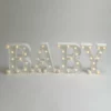 Napis BABY LED, zapalony. Białe litery 3D z napisem "BABY", z zamontowanymi żarówkami emitującymi ciepłe, żółtawe światło. Idealna dekoracja świetlna na baby shower, wesela, oraz inne eventy. Oświetlony napis dostępny w wypożyczalni dekoracji rent4events.pl we Wrocławiu. Litery stanowią doskonałą scenografię na ślubach i imprezach okolicznościowych. Sprawdź ofertę Rent4Weddings na rent4weddings.pl - rent4events.pl wypożycz wrażenia, rent4weddings.pl zachowaj wspomnienia.