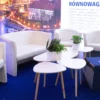 Elegancka aranżacja strefy wypoczynkowej/kawowej z białymi fotelami i sofą, uzupełniona o nowoczesne stoliki na drewnianych nogach oraz zielone rośliny w minimalistycznych doniczkach. Sceneria uzupełniona jest podświetlonym tłem z widokiem na panoramę Wrocławia. Niebieskie pufy z nadrukiem „WRO” dodają nowoczesnego charakteru i promują miasto. Doskonała scenografia na eventy biznesowe i promocyjne. Stylowe wyposażenie dostępne w ofercie wypożyczalni Rent4Events - rent4events.pl wypożycz wrażenia, rent4weddings.pl zachowaj wspomnienia. Fot. @karolinakiec_fotografia.