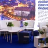 Ekskluzywna aranżacja strefy eventowej z plakatem z nocną panoramę Wrocławia w tle, podkreślona eleganckimi białymi fotelami, sofami i nowoczesnymi stolikami na drewnianych nogach. Niebieskie pufy z nadrukiem „WRO” oraz półki z zielonymi roślinami w minimalistycznych doniczkach tworzą przyjazną i stylową przestrzeń. Oświetlenie tła i hasło „Różnorodność, wszechstronność, równowaga” podkreślają promocyjny i biznesowy charakter miasta. Idealna scenografia na wydarzenia we Wrocławiu. Profesjonalne wyposażenie dostępne w Rent4Events - rent4events.pl wypożycz wrażenia, rent4weddings.pl zachowaj wspomnienia. Fot. @karolinakiec_fotografia.