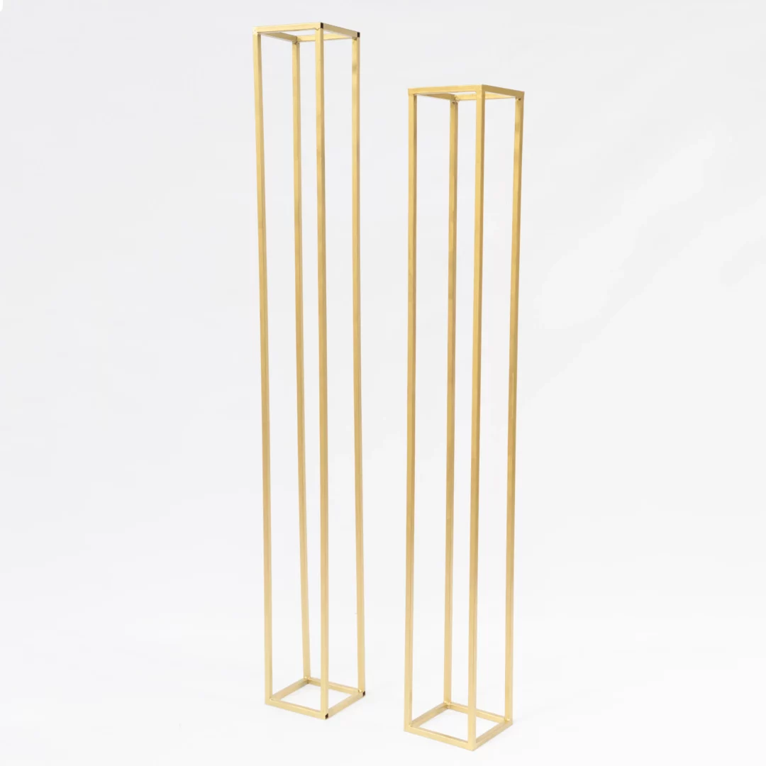 Złoty Słupek 205 i Złoty Słupek 225 cm. Zestaw dwóch złotych słupków dekoracyjnych o wysokościach 225 cm i 200 cm, z podstawą 25x25 cm. Minimalistyczny design wykonany ze stali doskonale pasuje do stylu glamour i romantycznego. Idealne do kompozycji kwiatowych i aranżacji przestrzeni podczas ślubów, wesel i eventów. Złoty kolor dodaje elegancji i prestiżu każdej dekoracji. Dostępne w wypożyczalni dekoracji we Wrocławiu – rent4events.pl oraz rent4weddings.pl - rent4events.pl wypożycz wrażenia, rent4weddings.pl zachowaj wspomnienia.