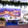 Stoisko eventowe „Wrocław – miasto spotkań” przygotowane przez wypożyczalnię rent4events.pl / rent4weddings.pl. Eleganckie białe meble, zielone rośliny w donicach, wiszące dekoracje i tło z panoramą miasta tworzą wyjątkową scenografię. Wypożyczalnia dekoracji oferuje kompleksowe wyposażenie i aranżacje, które podnoszą prestiż każdej uroczystości. Dla organizatorów ślubów, wesel i eventów we Wrocławiu i okolicach rent4events.pl i rent4weddings.pl to gwarancja stylu i jakości - rent4events.pl wypożycz wrażenia, rent4weddings.pl zachowaj wspomnienia. Fot. @karolinakiec_fotografia.