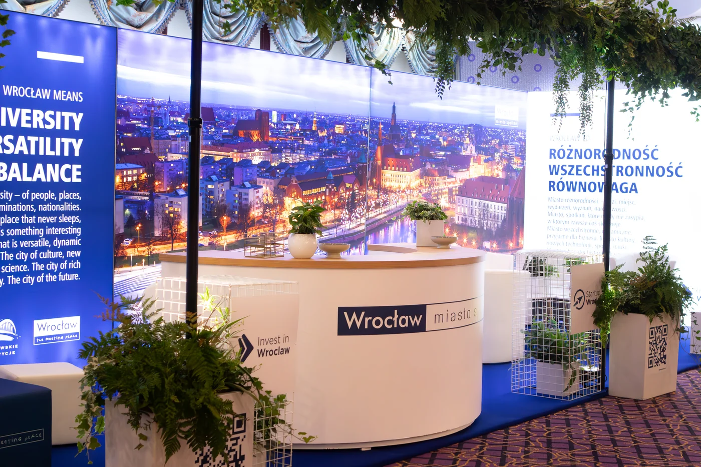 przetrzen eventowa stoisko targowe recepcja eventy wypozyczalnia dekoracji rent4events rent4wedding wroclaw - Wypożyczalnia Ślubna Stoisko eventowe „Wrocław – miasto spotkań” zrealizowane przez rent4events.pl / rent4weddings.pl. Elegancka lada, białe stelaże, zielone dekoracje roślinne oraz podświetlana panorama miasta tworzą niezwykłe wrażenie. Dekoracje, branding i elementy multimedialne przygotowane przez wypożyczalnię pozwalają zbudować przestrzeń, która podkreśla wartości miasta: różnorodność, wszechstronność i równowagę. Wypożyczalnia rent4events.pl oraz rent4weddings.pl – to gwarancja niezapomnianego wydarzenia - rent4events.pl wypożycz wrażenia, rent4weddings.pl zachowaj wspomnienia. Fot. @karolinakiec_fotografia.